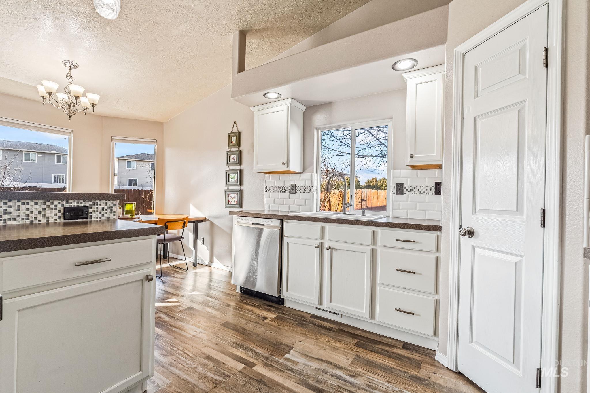 Kitchen with white cabinets, stainless steel dishwasher, dark wood-style flooring, a textured ceiling, and plenty of natural light