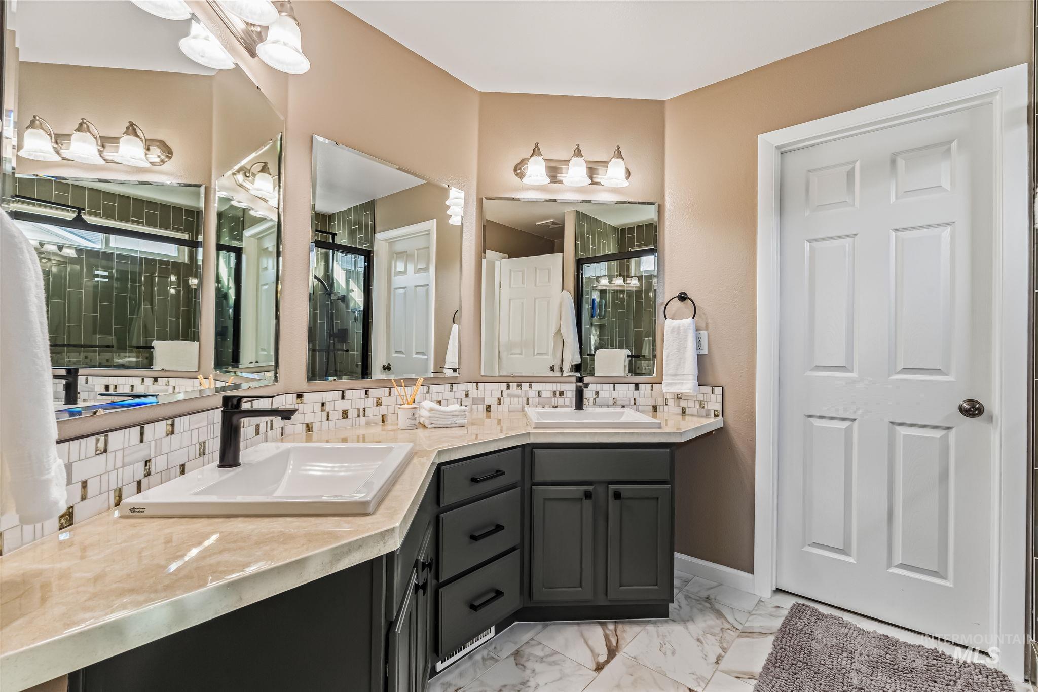 Full bath featuring double vanity, light marble finish floors, and decorative backsplash