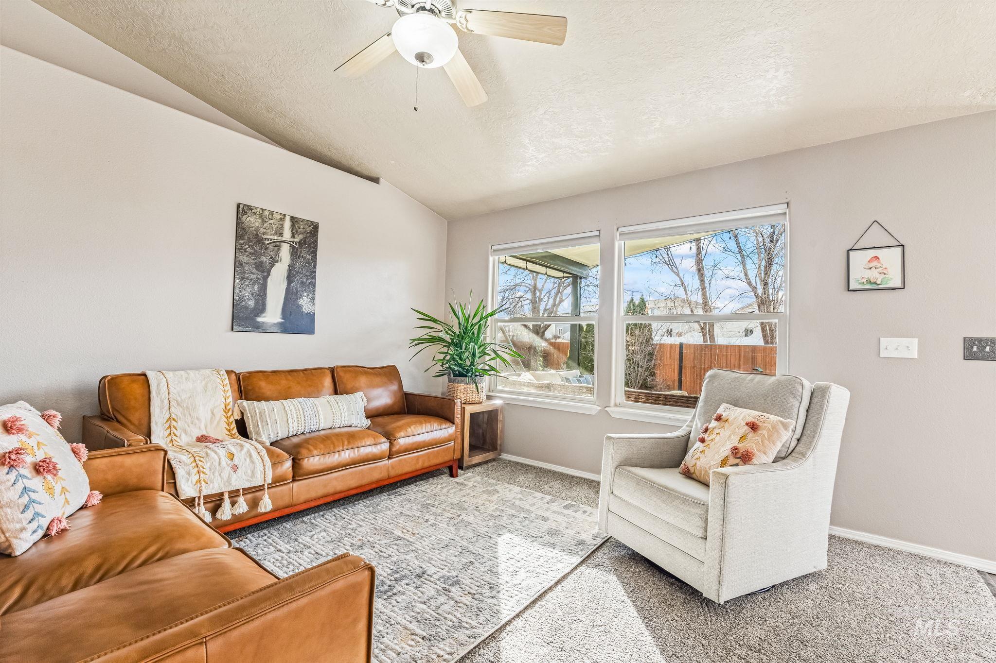 Living area featuring vaulted ceiling, carpet, a textured ceiling, and ceiling fan
