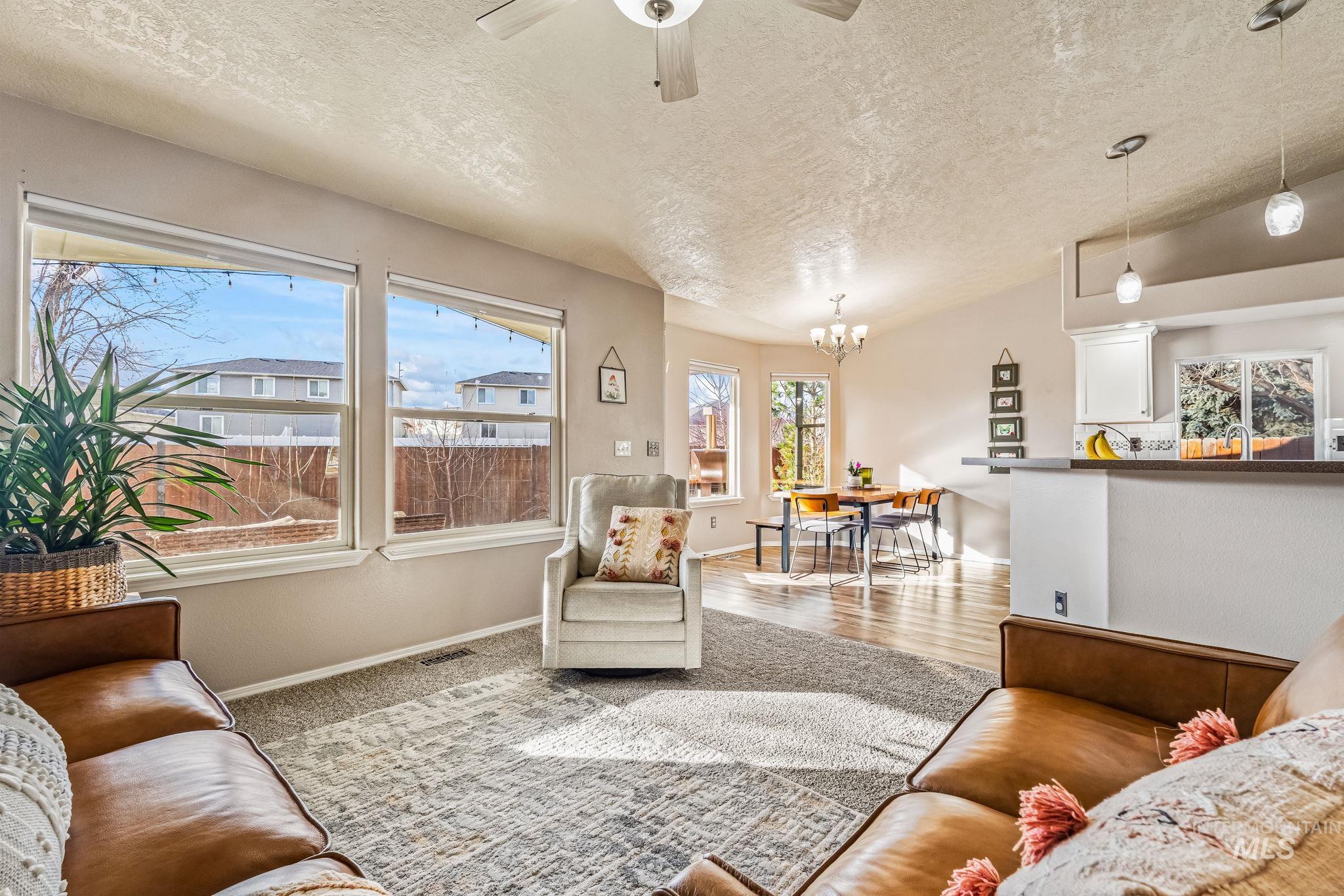 Living room featuring a textured ceiling, a ceiling fan, a chandelier, and vaulted ceiling