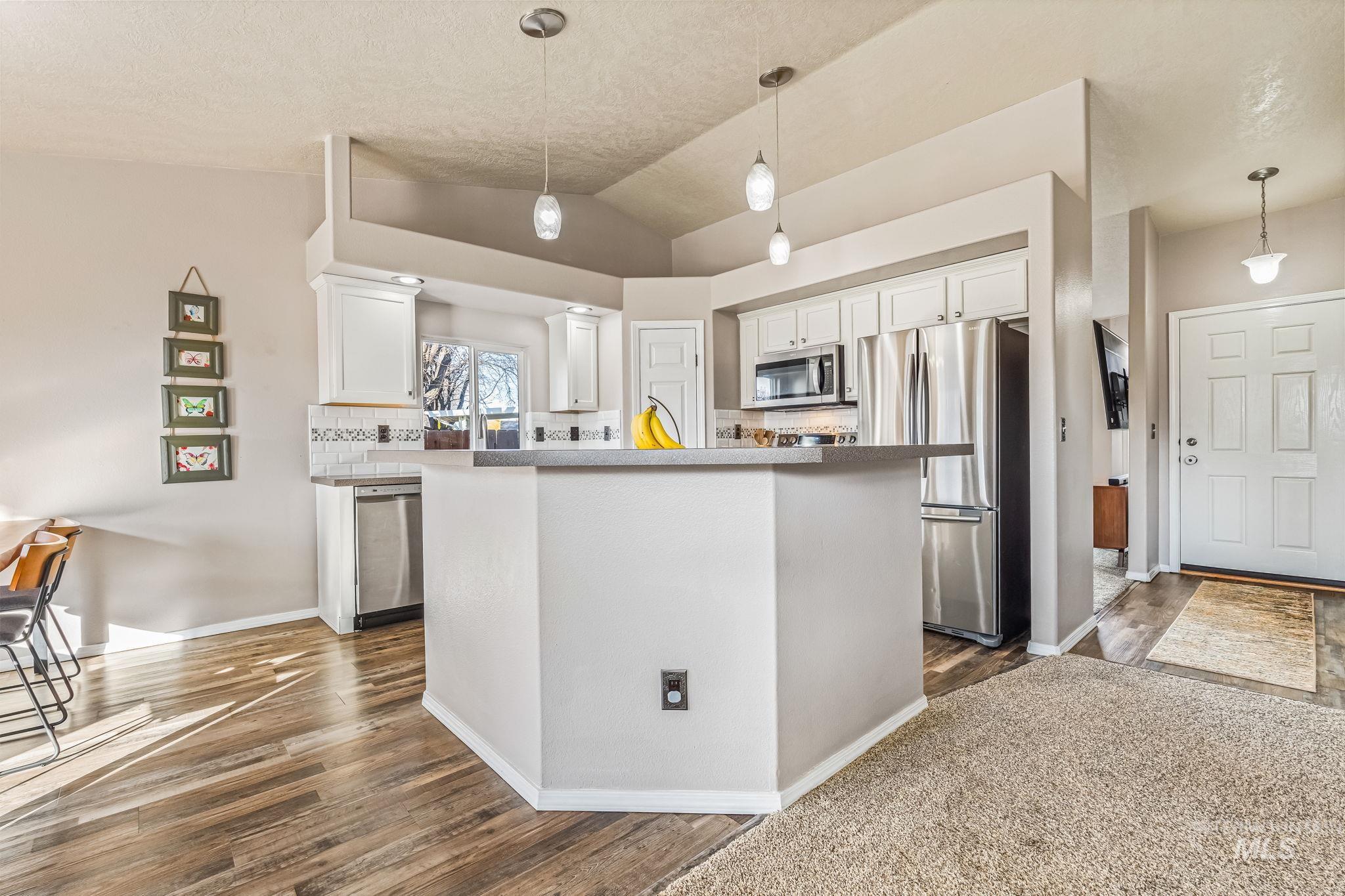 Kitchen featuring stainless steel appliances, hanging light fixtures, vaulted ceiling, white cabinets, and a center island