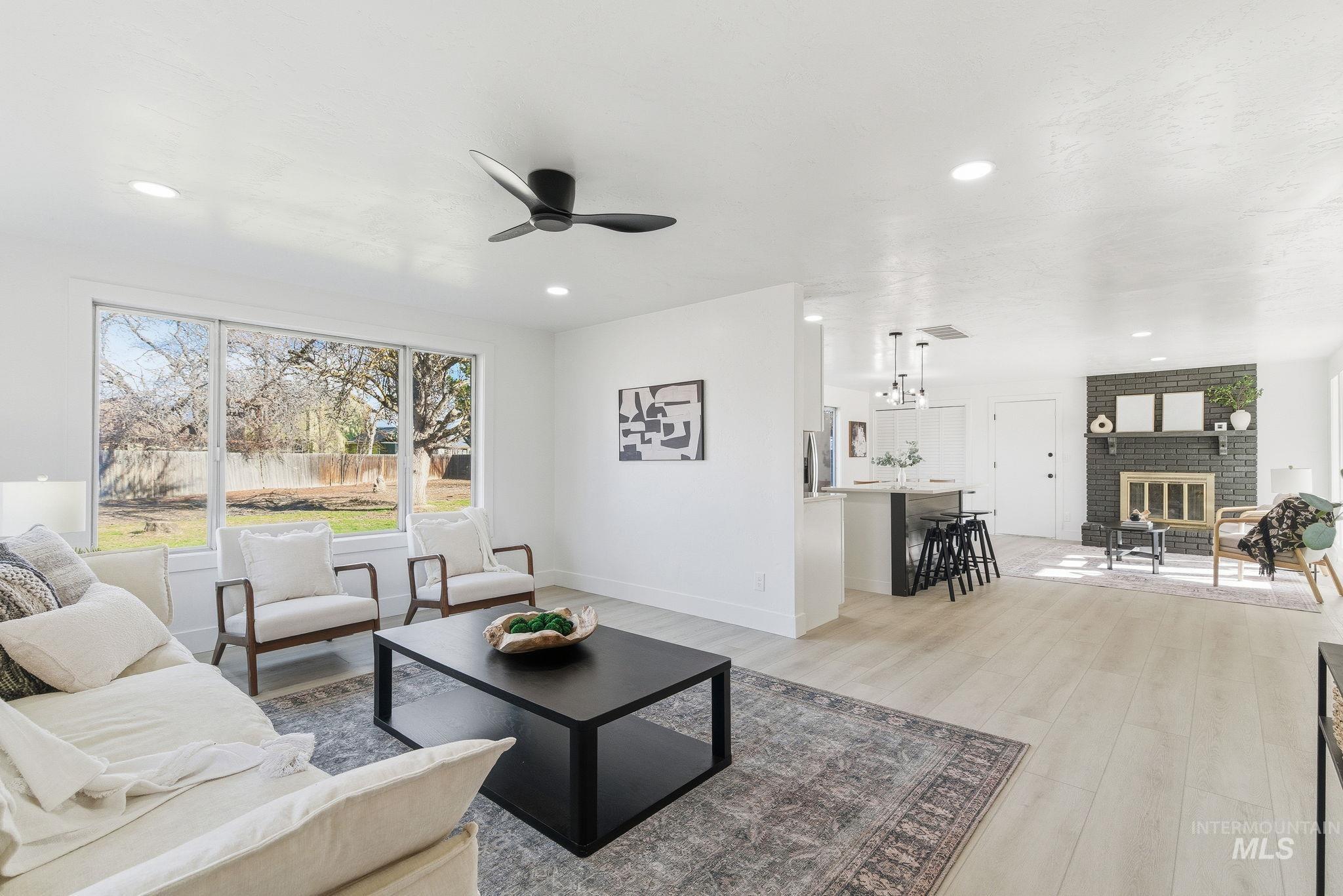 Living room with a brick fireplace, light wood-type flooring, ceiling fan, and recessed lighting