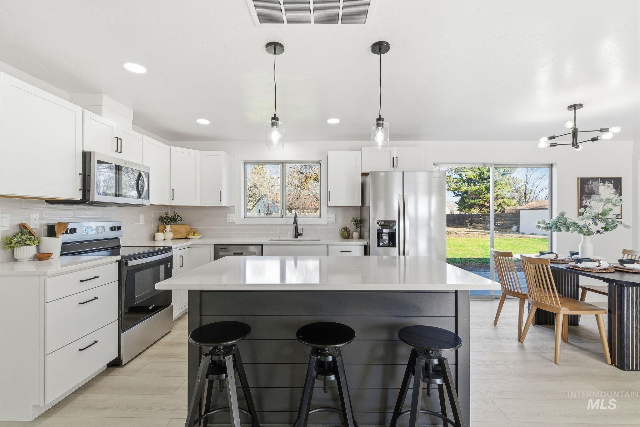 Kitchen featuring stainless steel appliances, decorative light fixtures, a center island, tasteful backsplash, and a kitchen breakfast bar
