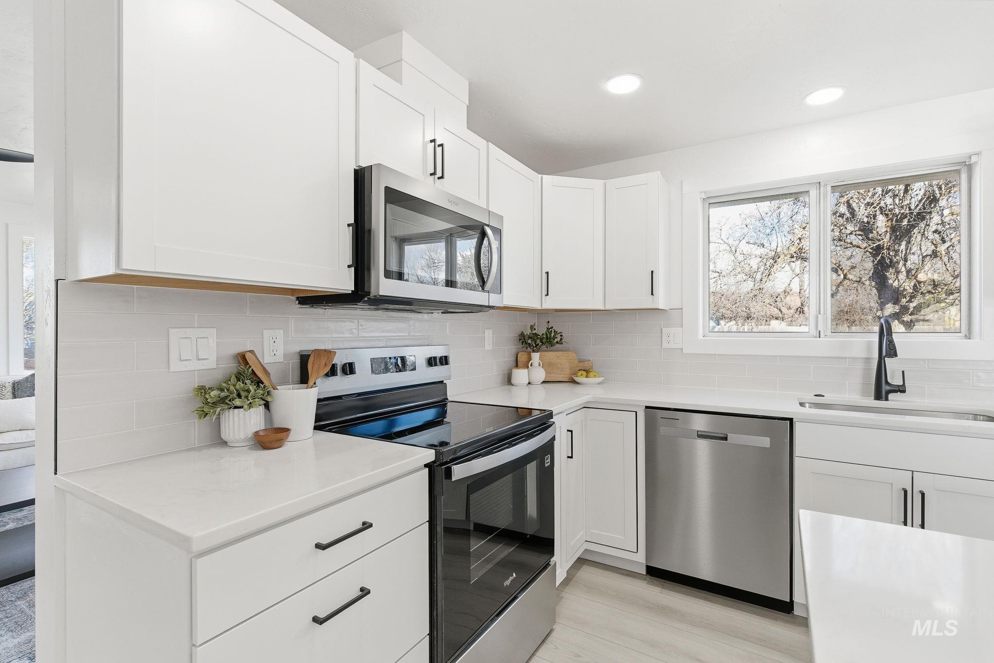 Kitchen with appliances with stainless steel finishes, decorative backsplash, white cabinetry, light stone countertops, and light wood-type flooring