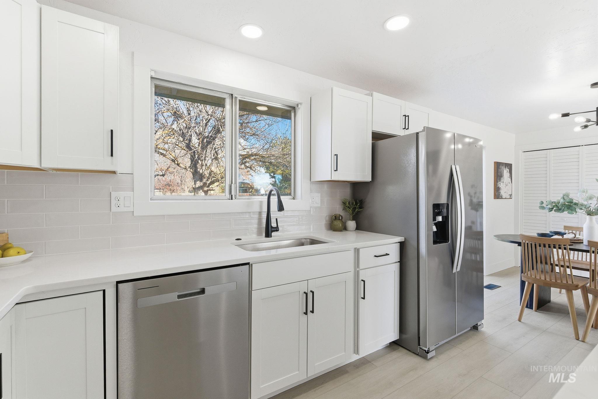 Kitchen featuring stainless steel appliances, white cabinetry, tasteful backsplash, and light stone counters
