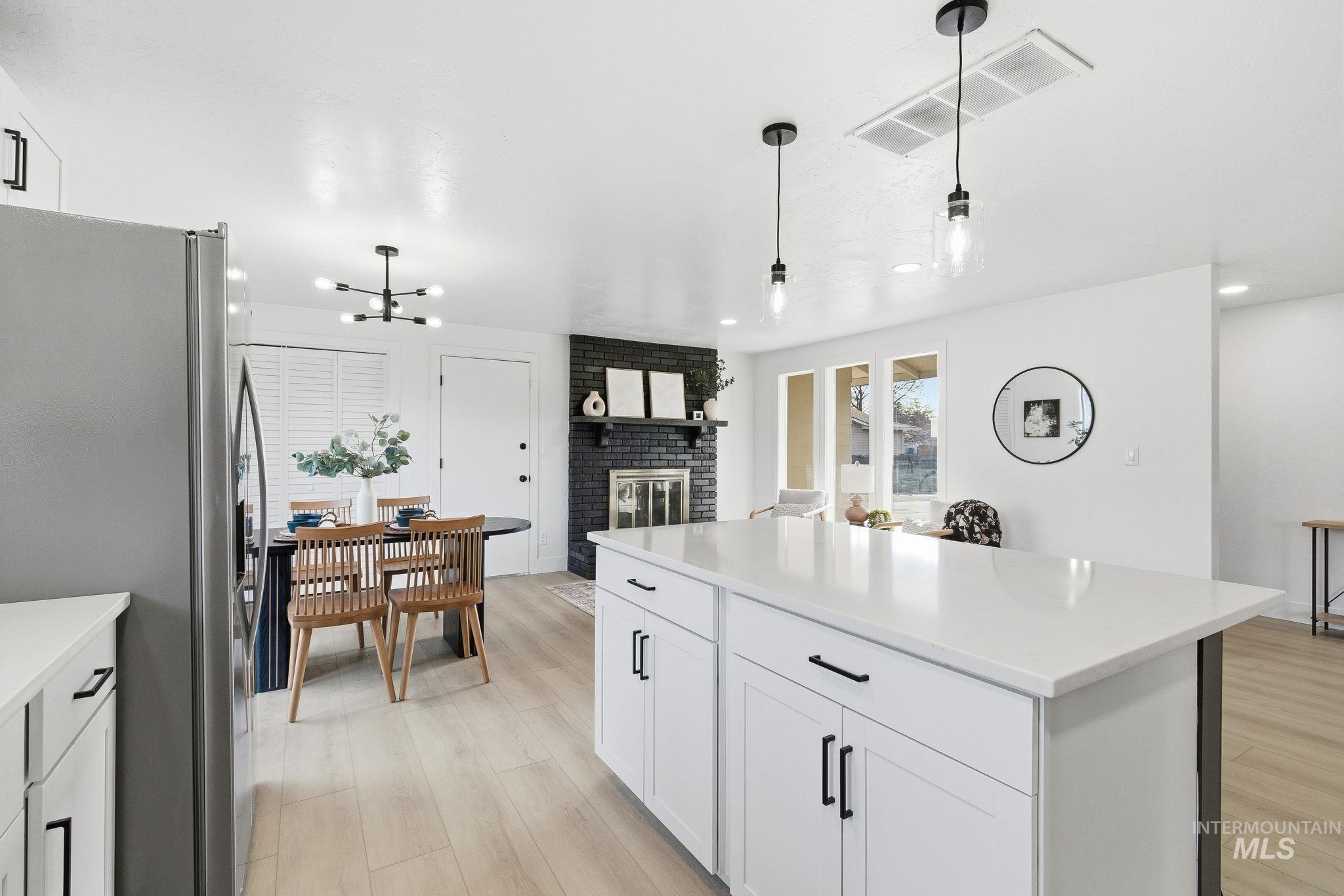 Kitchen with white cabinets, stainless steel fridge, hanging light fixtures, a center island, and light wood-style floors