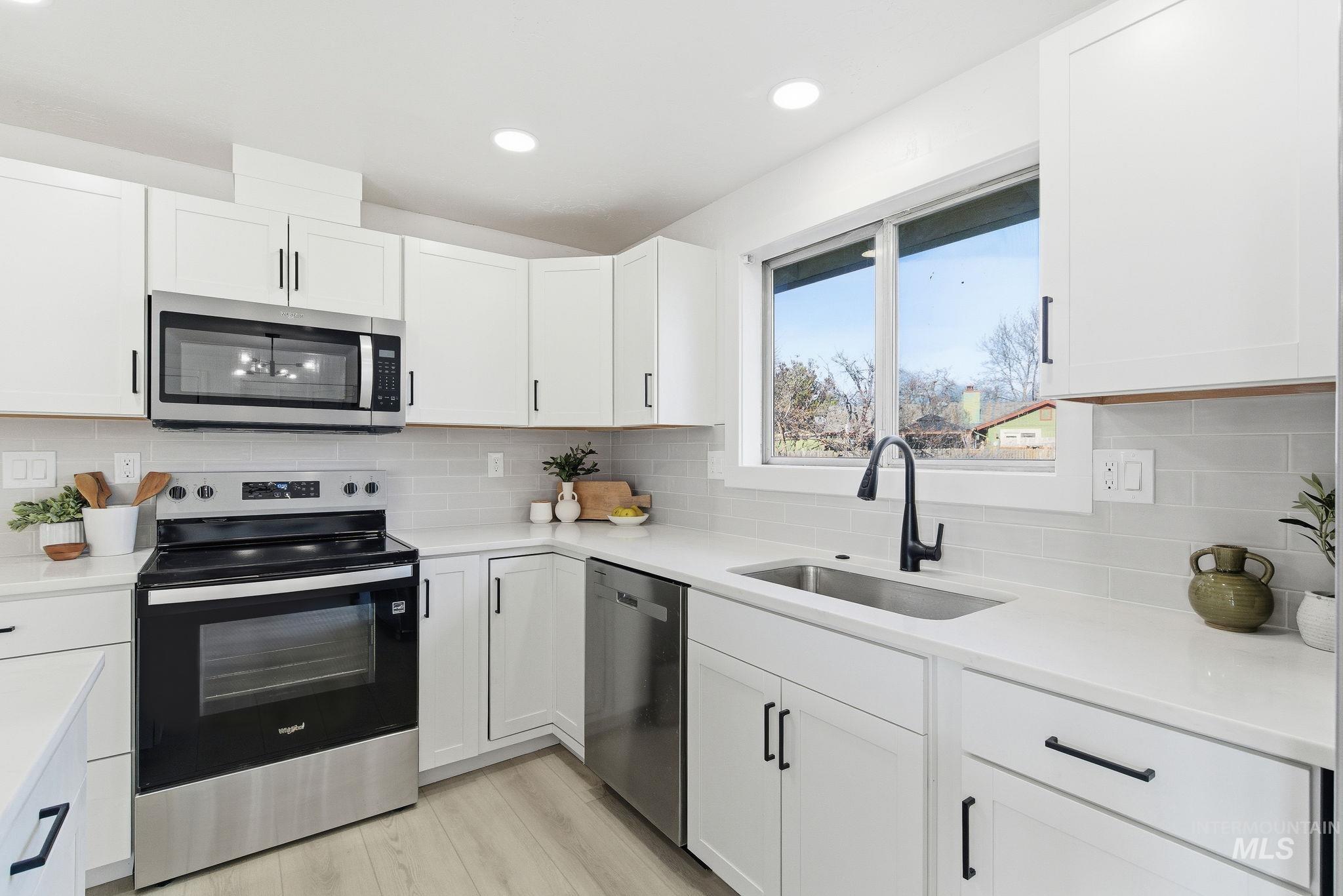 Kitchen featuring stainless steel appliances, white cabinetry, backsplash, light wood-style floors, and light stone counters