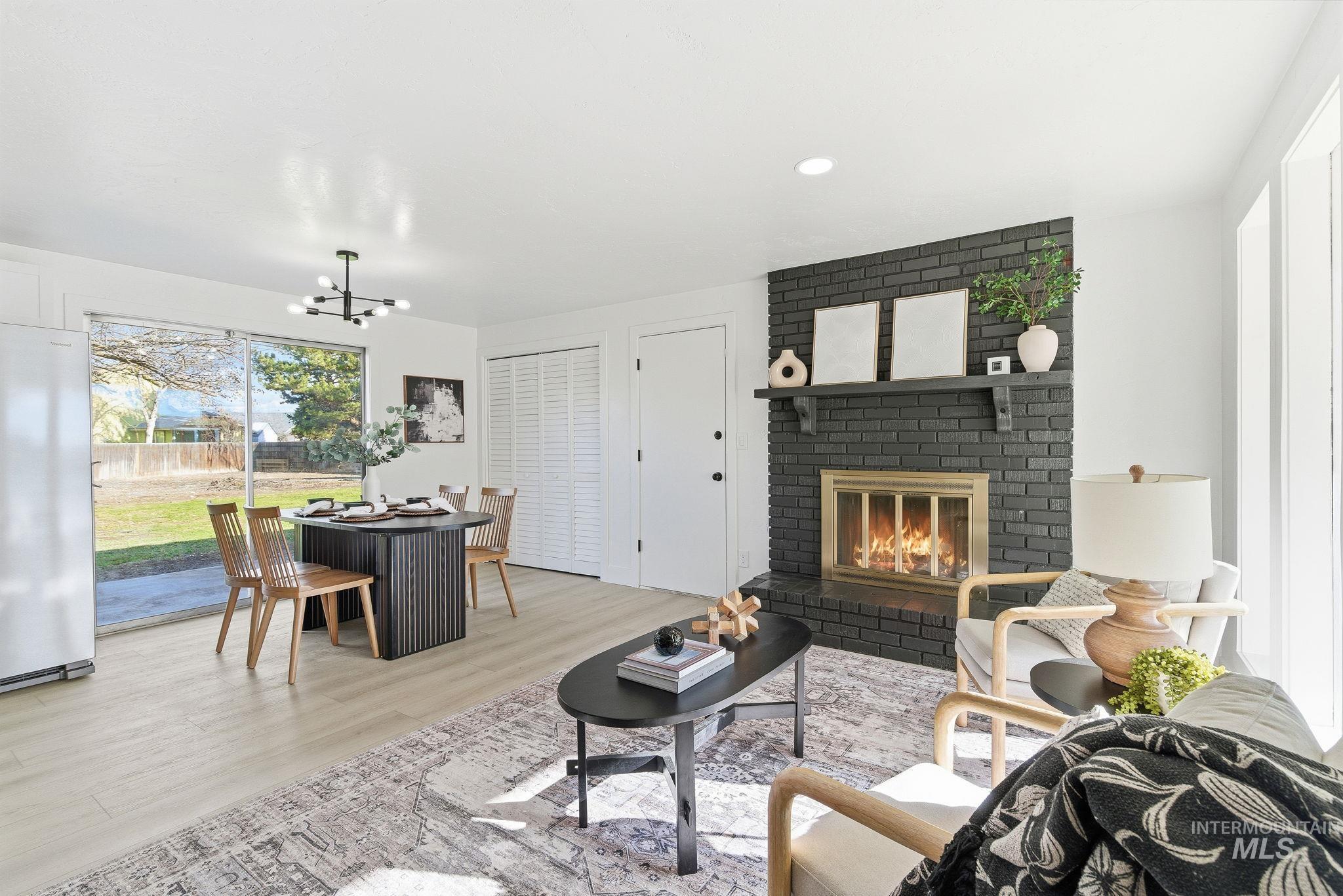 Living area featuring a brick fireplace, light wood-style flooring, and a chandelier