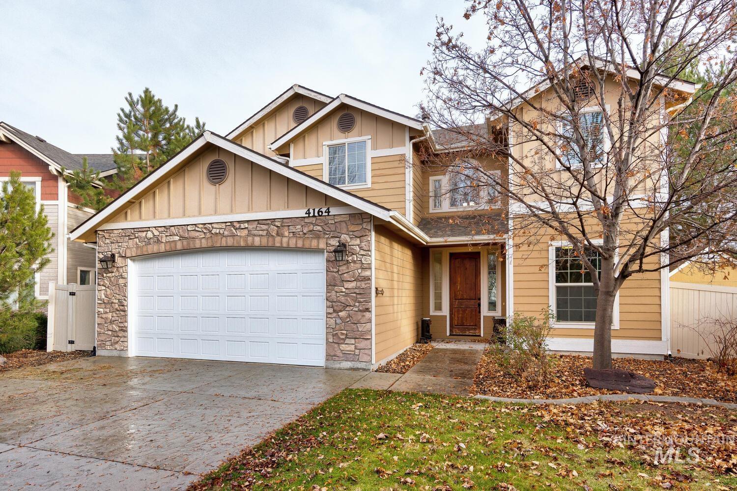 Craftsman-style house with board and batten siding, stone siding, driveway, and an attached garage
