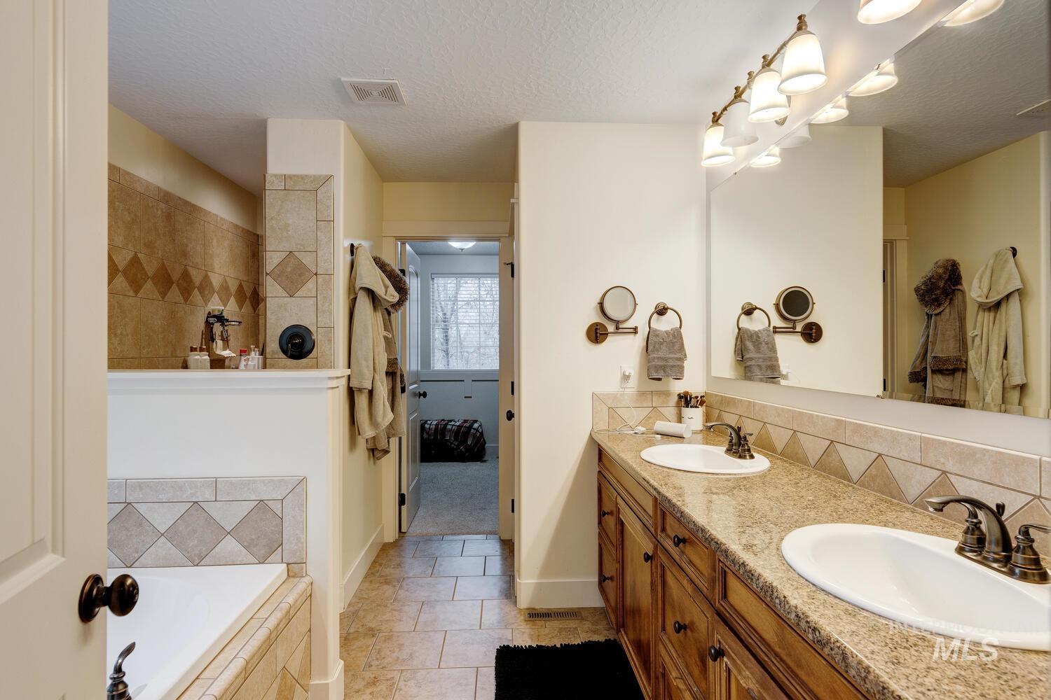 Bathroom featuring double vanity, decorative backsplash, a textured ceiling, a relaxing tiled tub, and light tile patterned floors