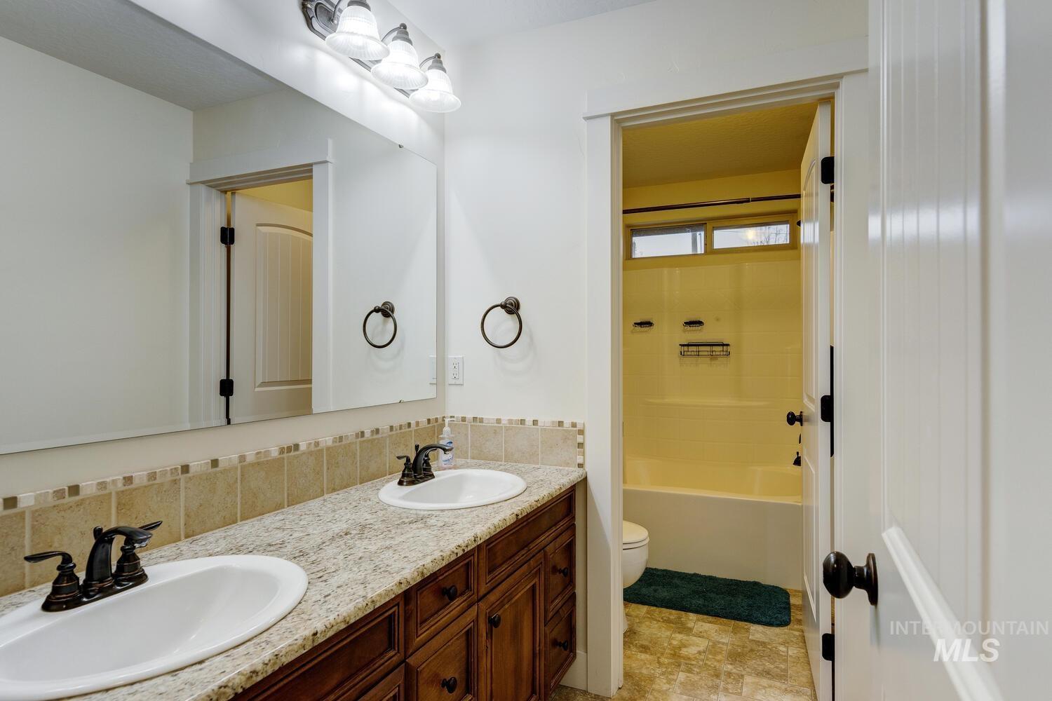 Full bath featuring double vanity, shower / washtub combination, and tasteful backsplash