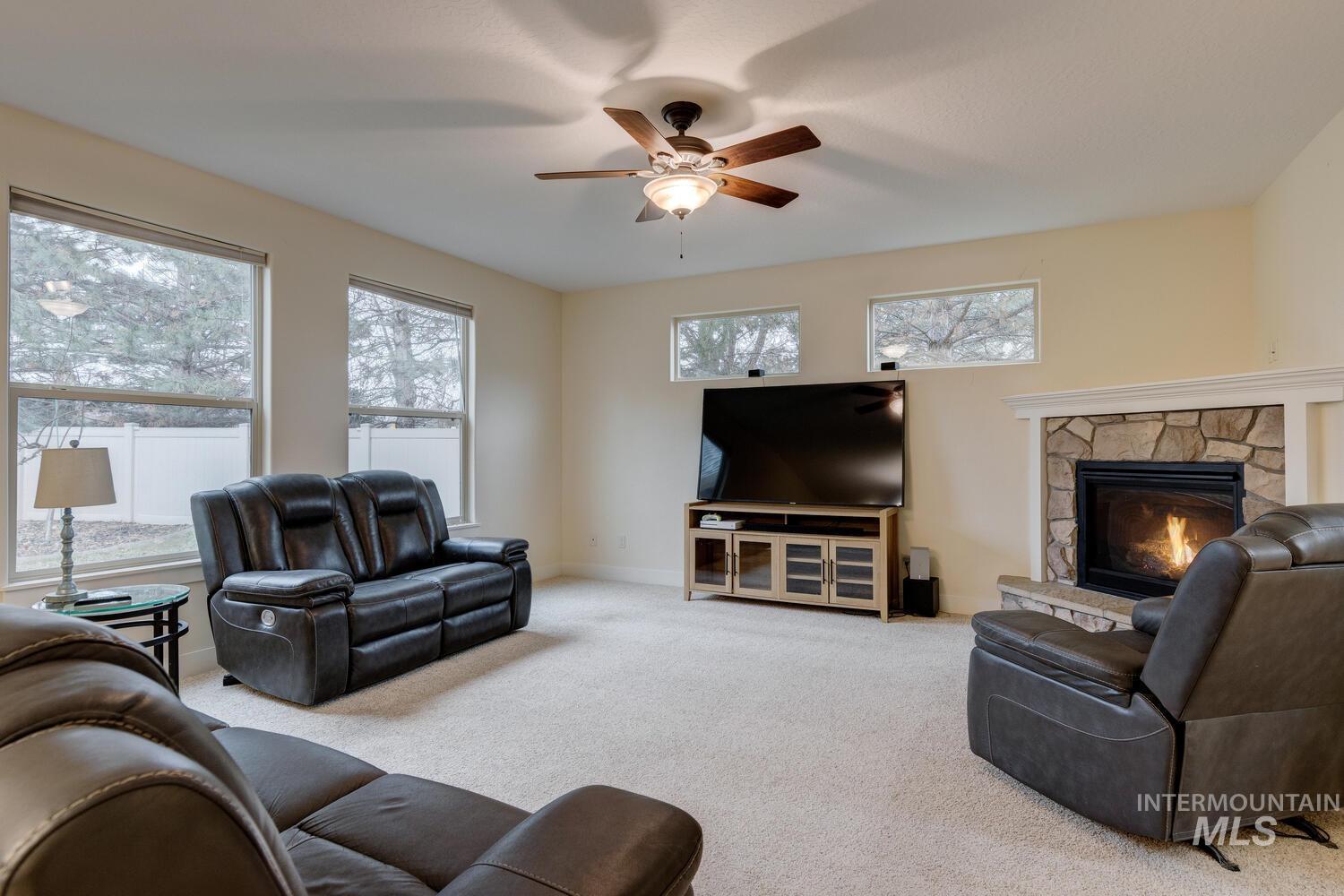 Living room featuring carpet, a fireplace, a ceiling fan, and plenty of natural light