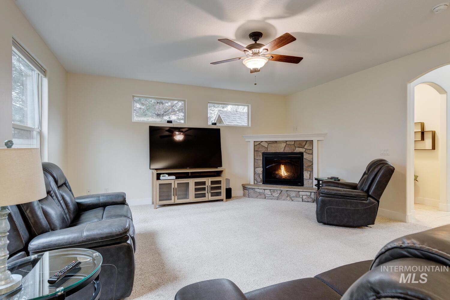 Living area with a stone fireplace, light carpet, a ceiling fan, and arched walkways