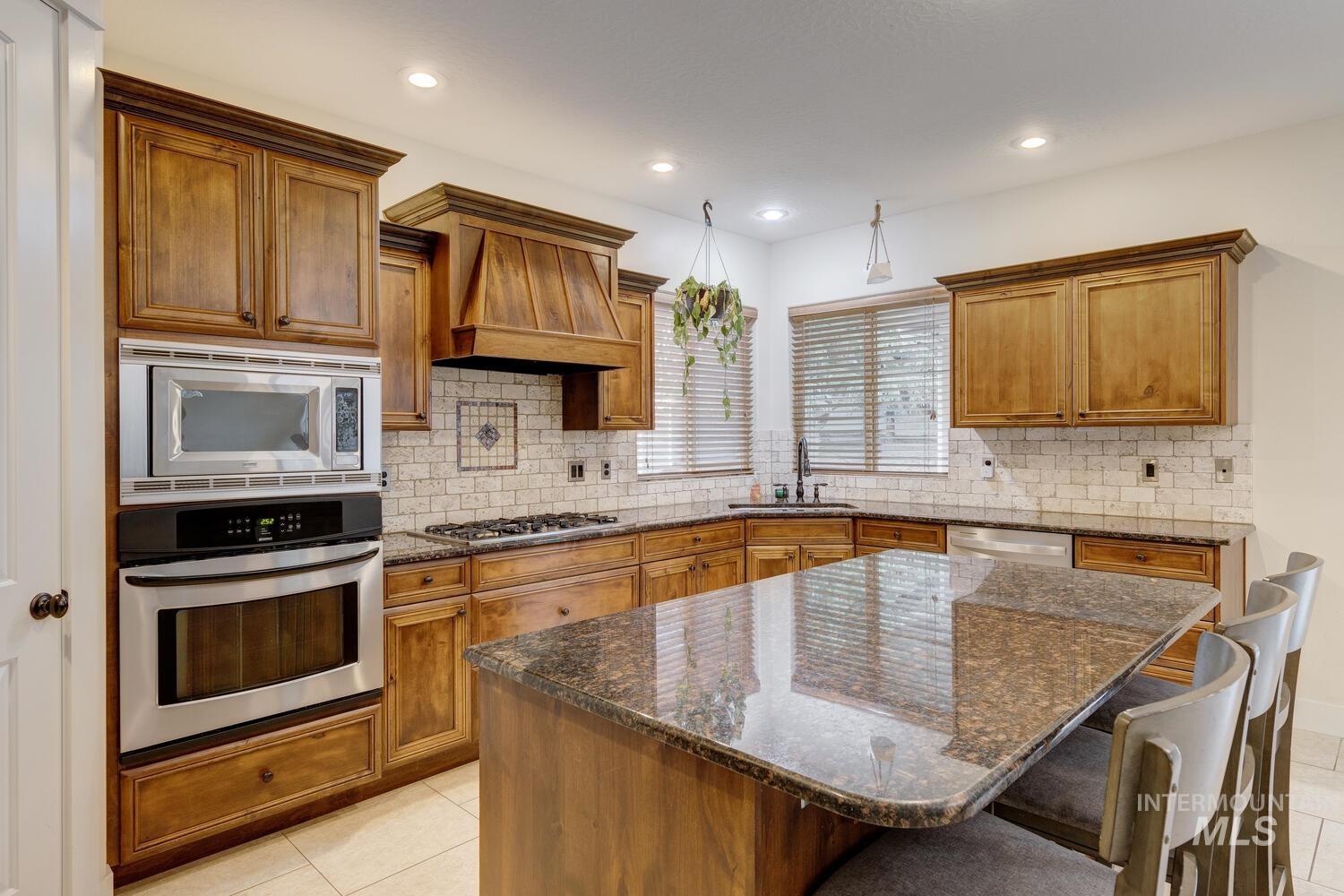 Kitchen featuring dark stone counters, brown cabinetry, appliances with stainless steel finishes, a breakfast bar, and recessed lighting