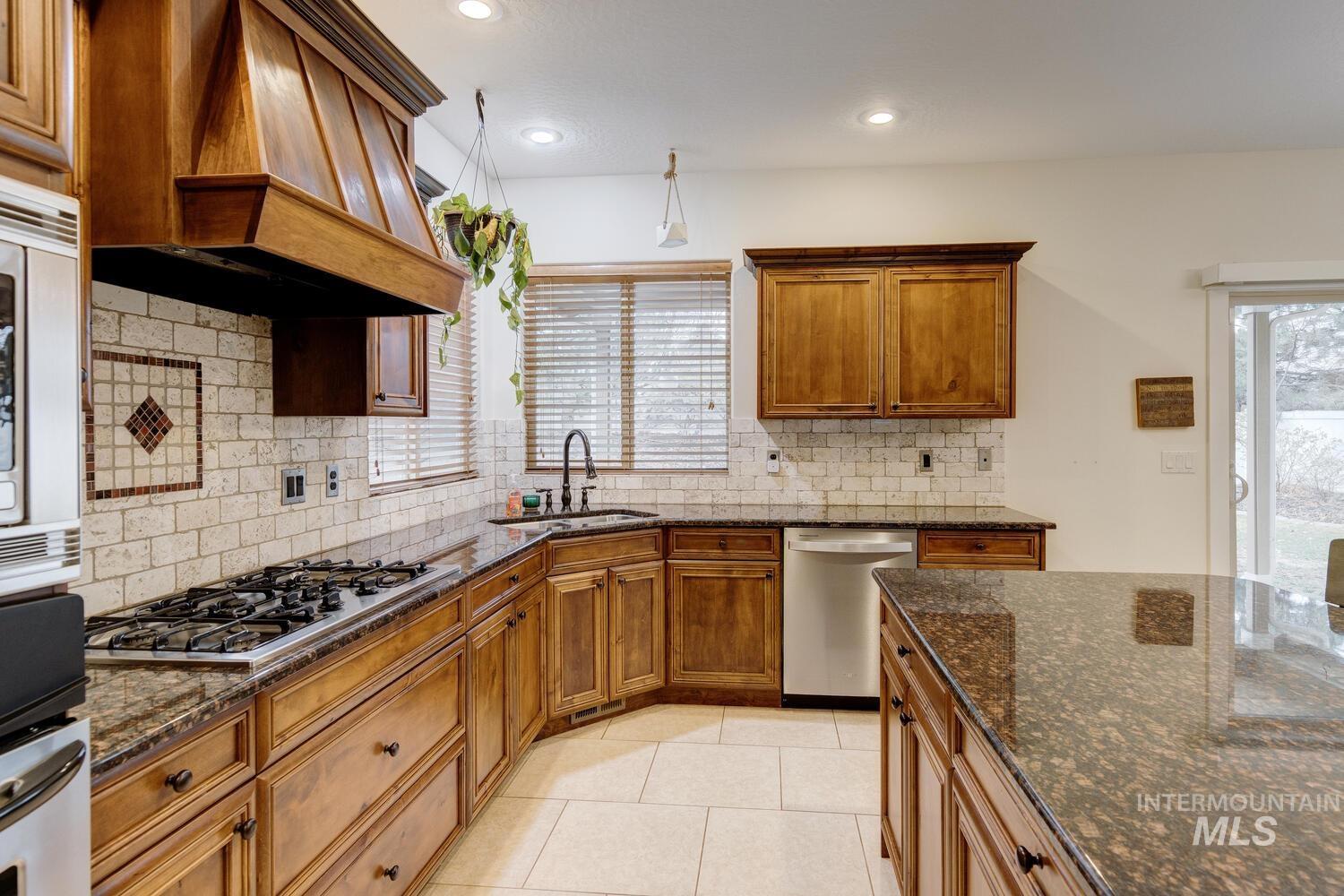 Kitchen with brown cabinetry, dark stone counters, stainless steel appliances, backsplash, and recessed lighting