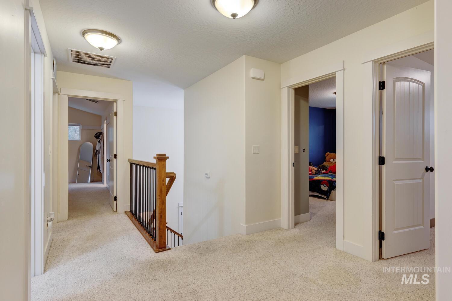Corridor with an upstairs landing, light carpet, and a textured ceiling