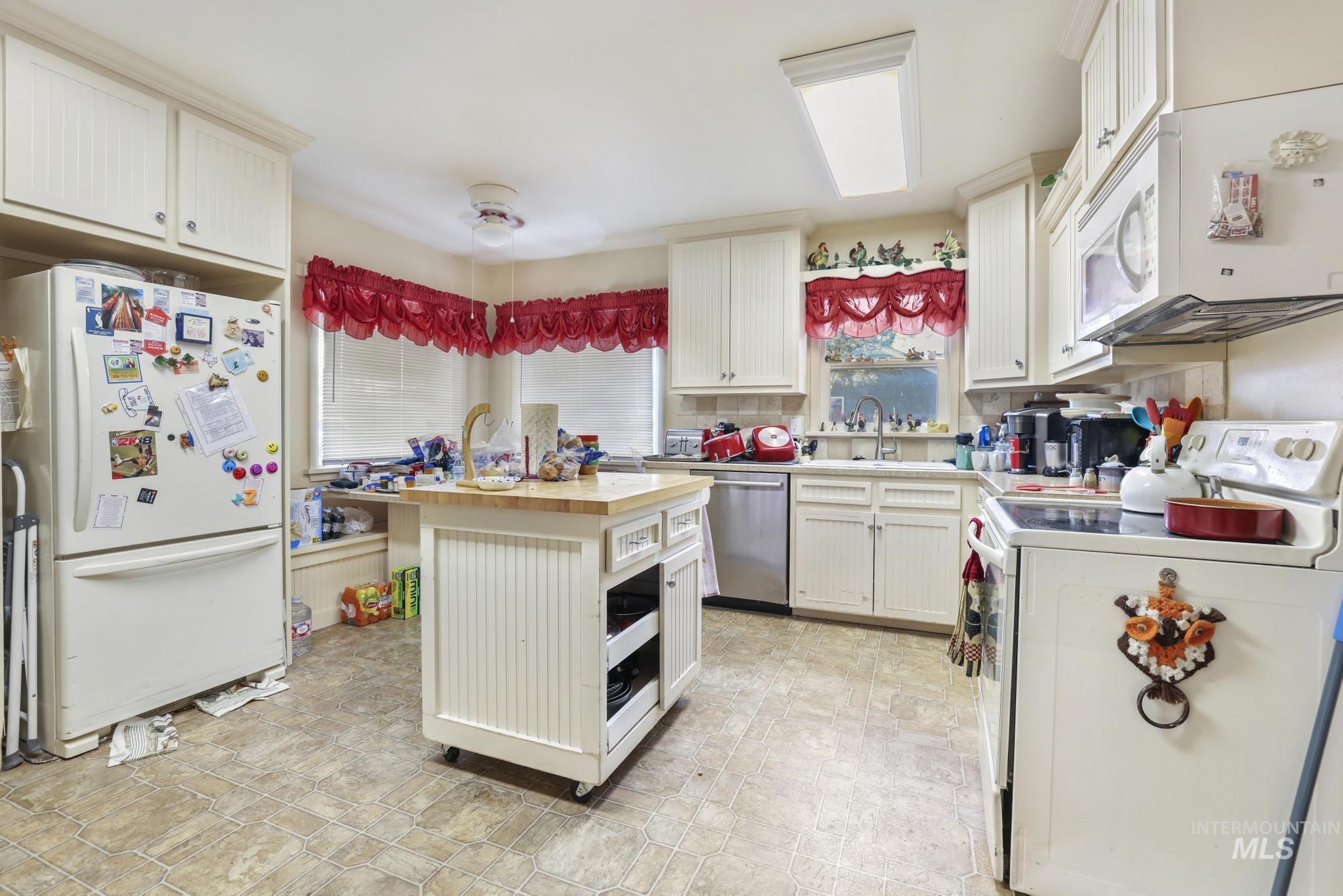 Kitchen featuring white appliances, a kitchen island with sink, wooden counters, and white cabinets