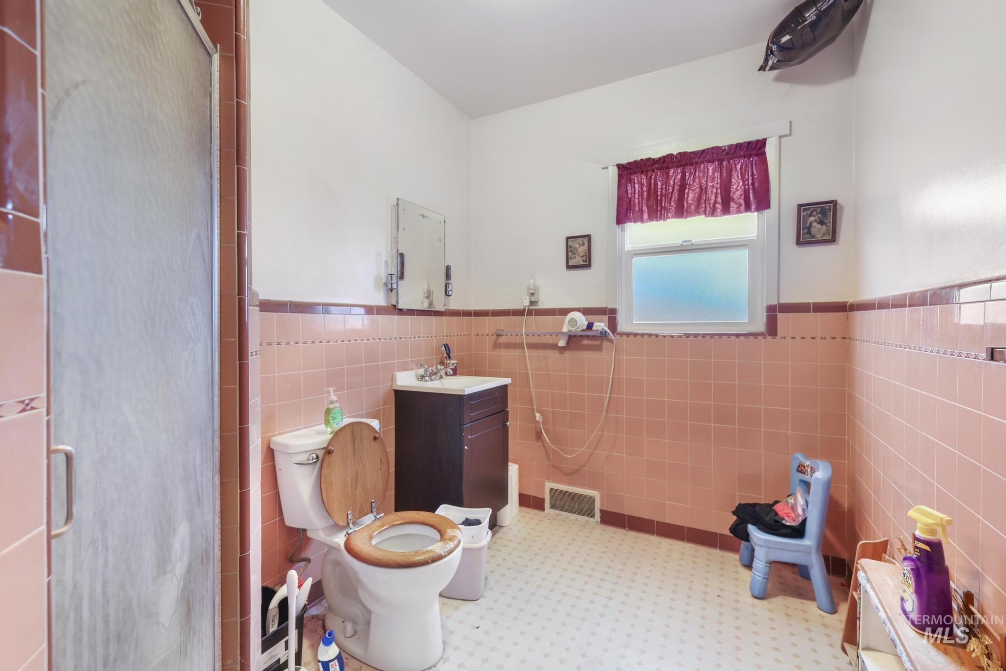 Full bathroom featuring a wainscoted wall, vanity, tile walls, and a stall shower