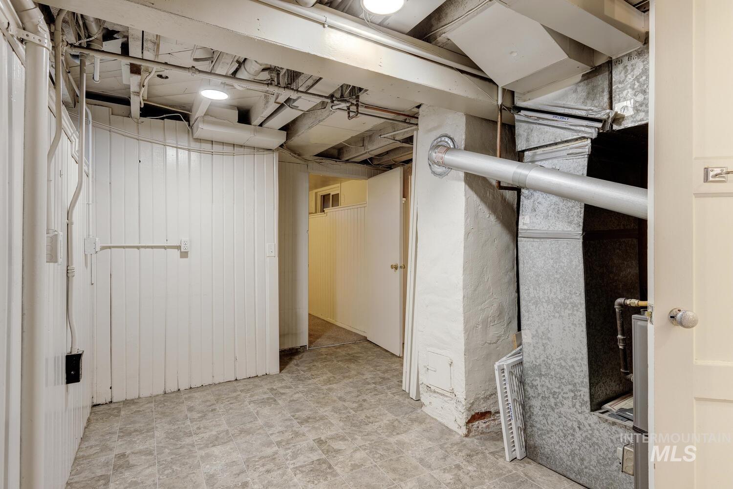Unfinished below grade area featuring wood walls, heating unit, and tile patterned floors