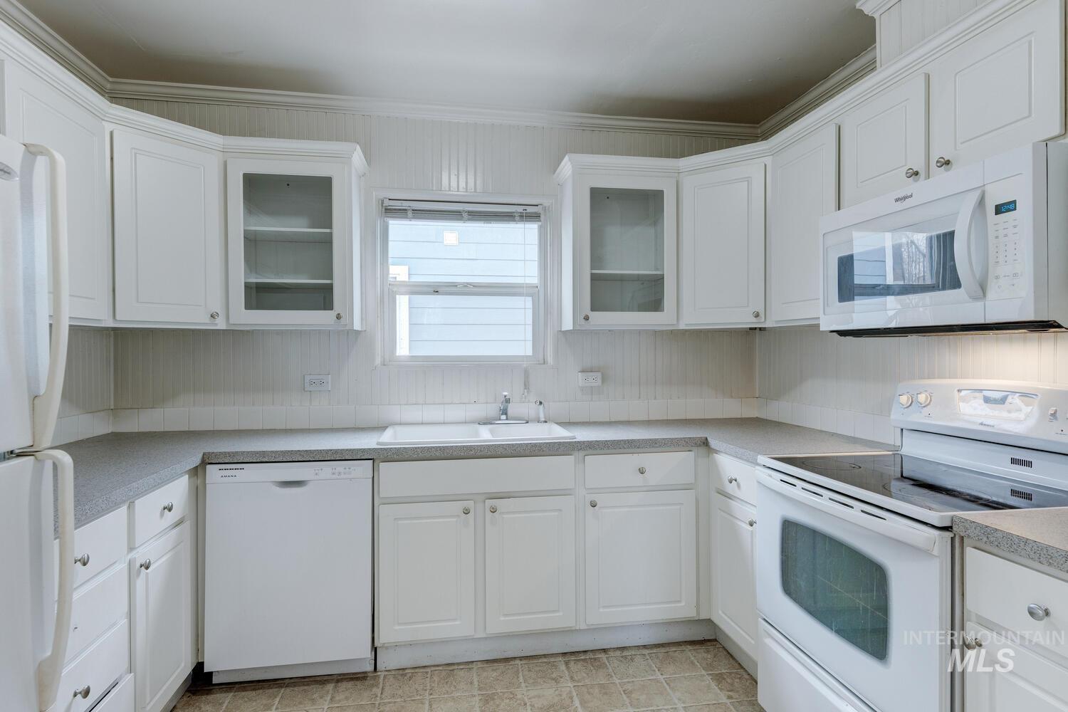 Kitchen featuring white appliances, white cabinets, glass insert cabinets, and light countertops