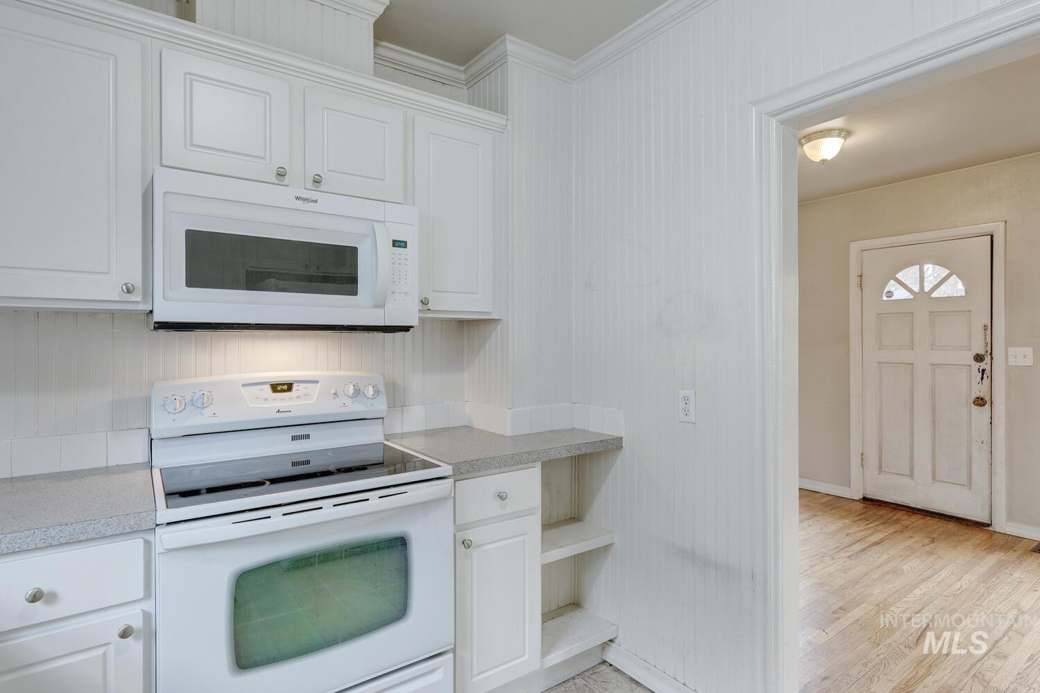 Kitchen with white appliances, light countertops, white cabinetry, light wood finished floors, and crown molding