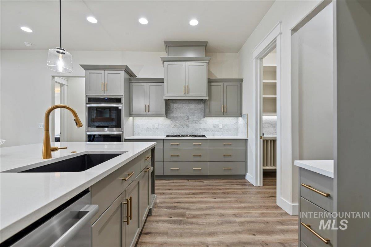 Kitchen with gray cabinets, hanging light fixtures, light wood-type flooring, appliances with stainless steel finishes, and recessed lighting