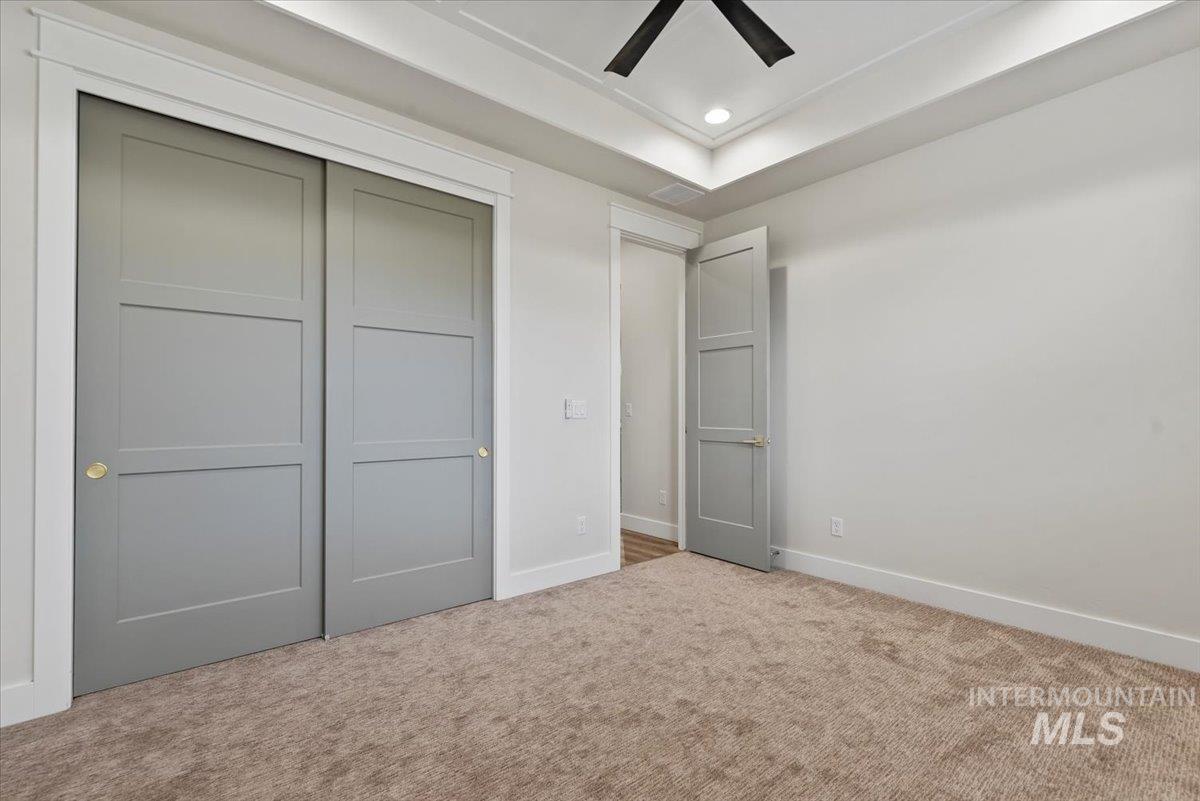 Unfurnished bedroom featuring a closet, carpet floors, recessed lighting, ceiling fan, and a tray ceiling