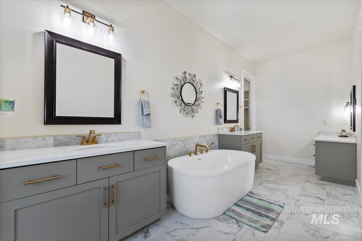 Full bath with a freestanding tub, light marble finish flooring, and two vanities