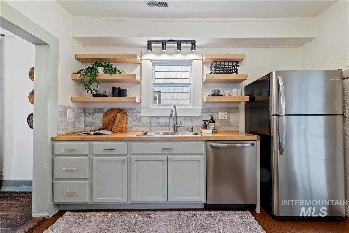 Kitchen featuring appliances with stainless steel finishes, tasteful backsplash, open shelves, wood counters, and dark wood-style flooring