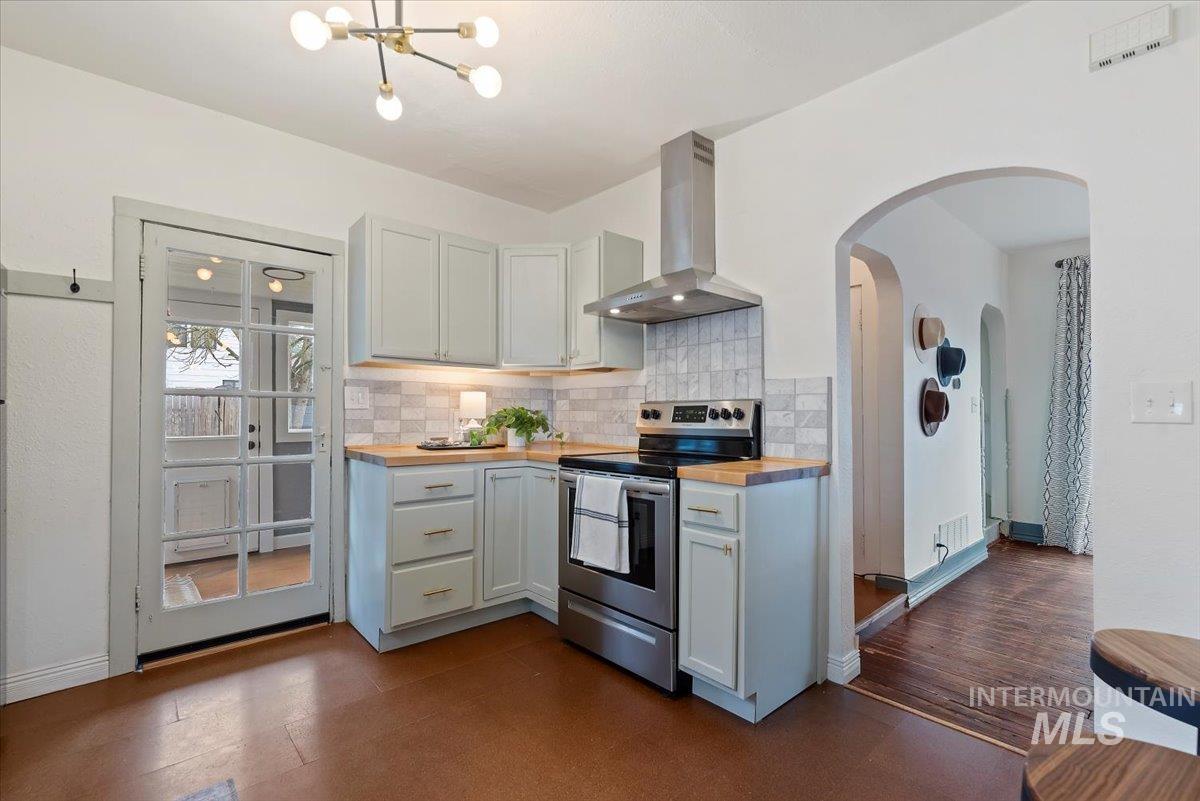 Kitchen with wooden counters, electric stove, wall chimney exhaust hood, and arched walkways