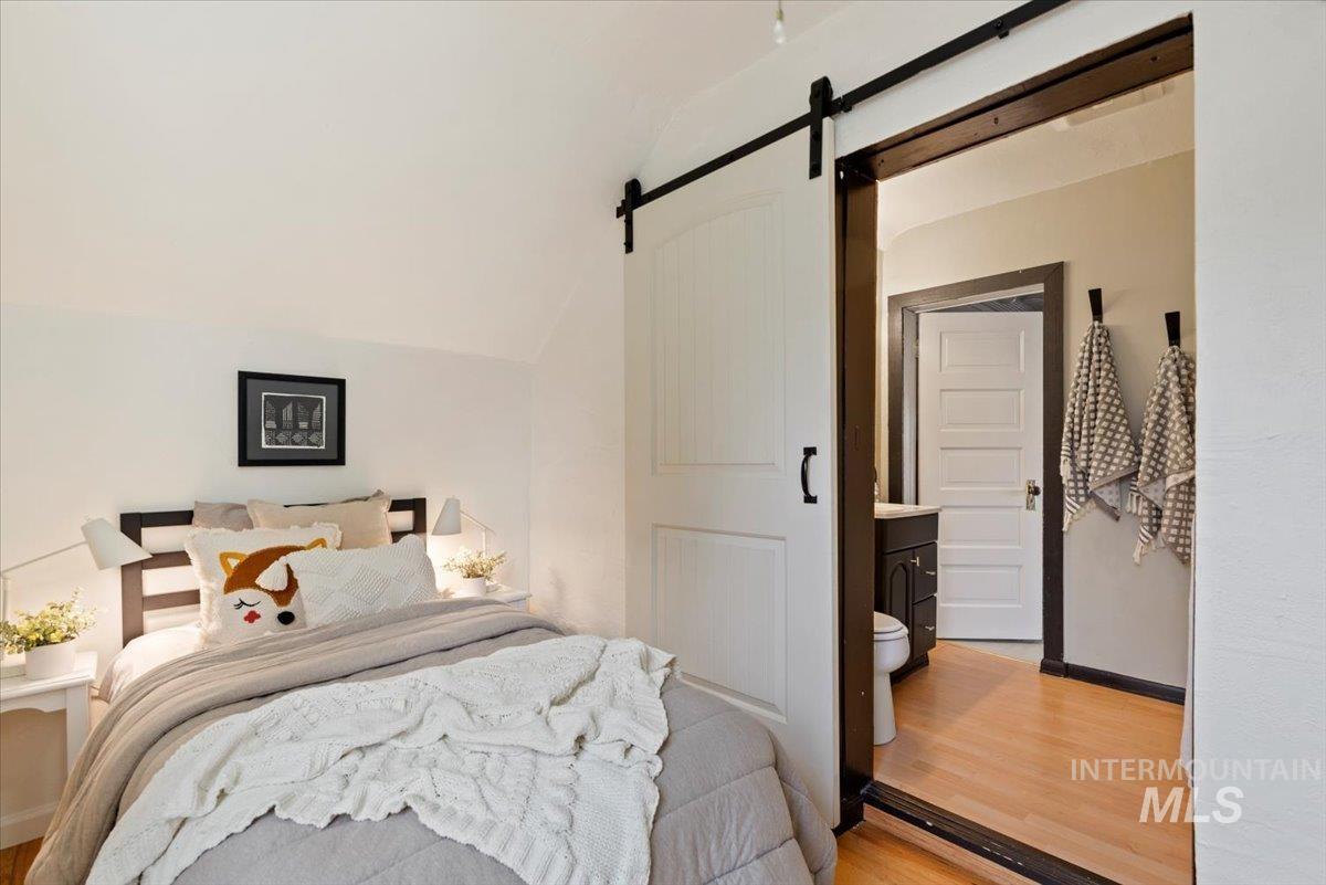 Bedroom featuring lofted ceiling, a barn door, wood finished floors, and connected bathroom