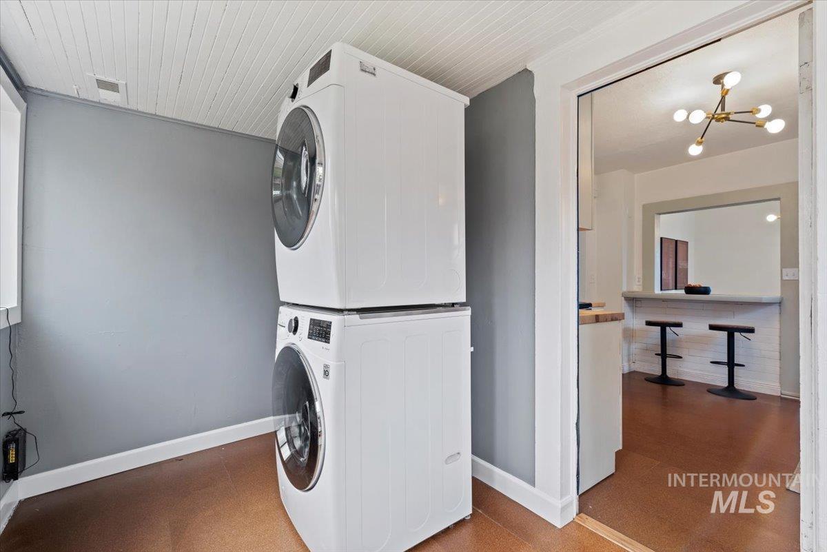 Laundry room with stacked washer / drying machine, a chandelier, and wood ceiling