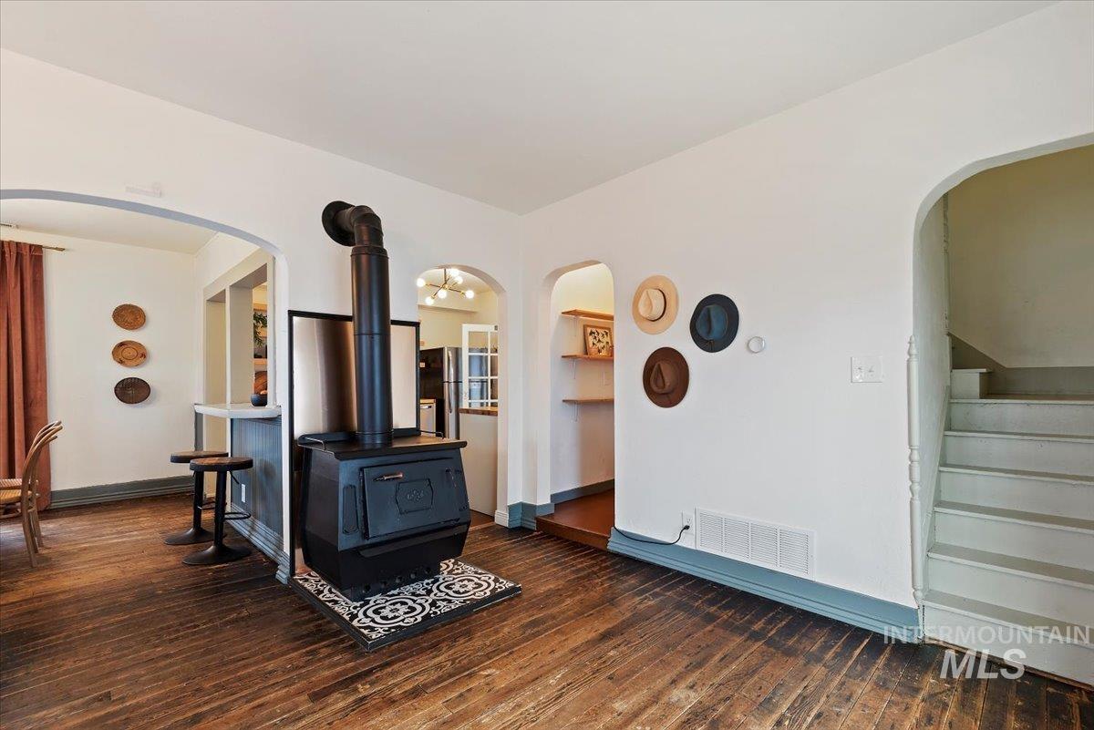 Living room with arched walkways, a wood stove, stairway, and dark wood-style flooring