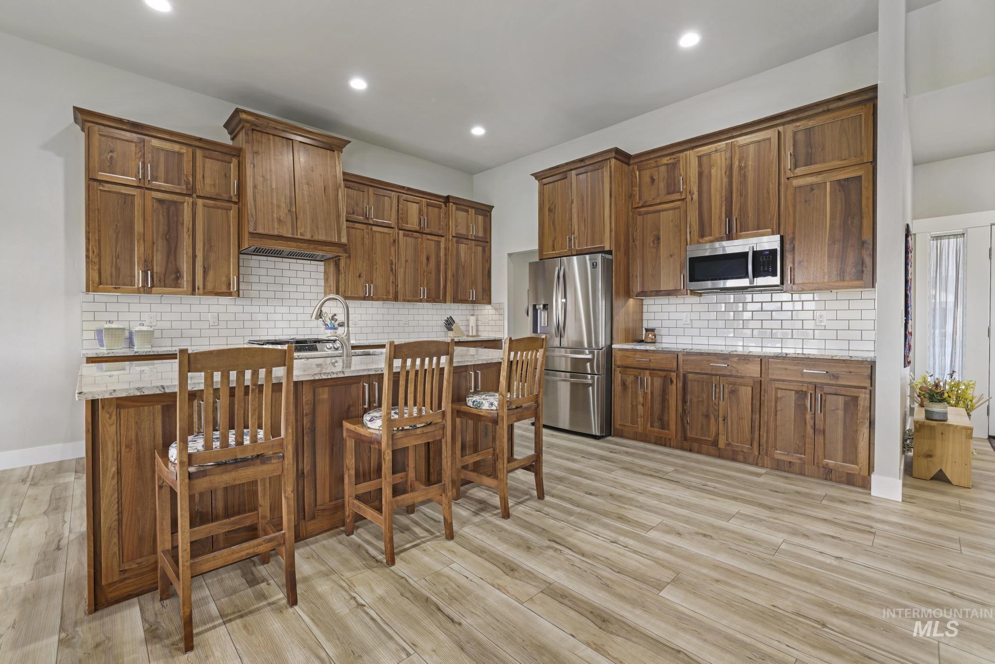 Kitchen featuring an island with sink, a kitchen bar, stainless steel appliances, light stone countertops, and tasteful backsplash