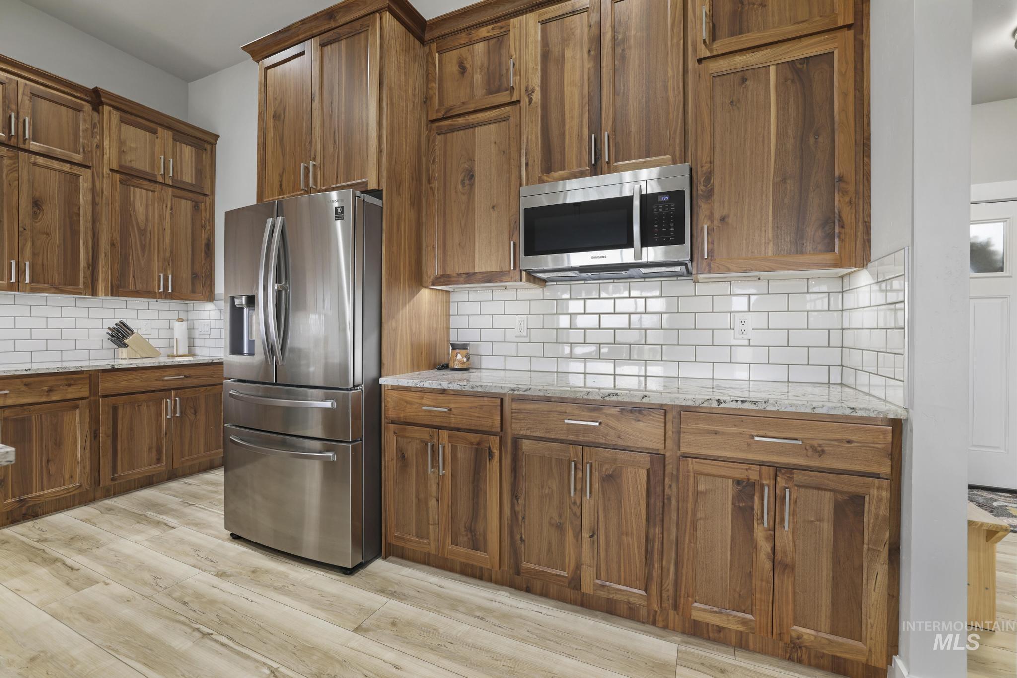 Kitchen with stainless steel appliances, light stone counters, light wood-style floors, brown cabinetry, and decorative backsplash