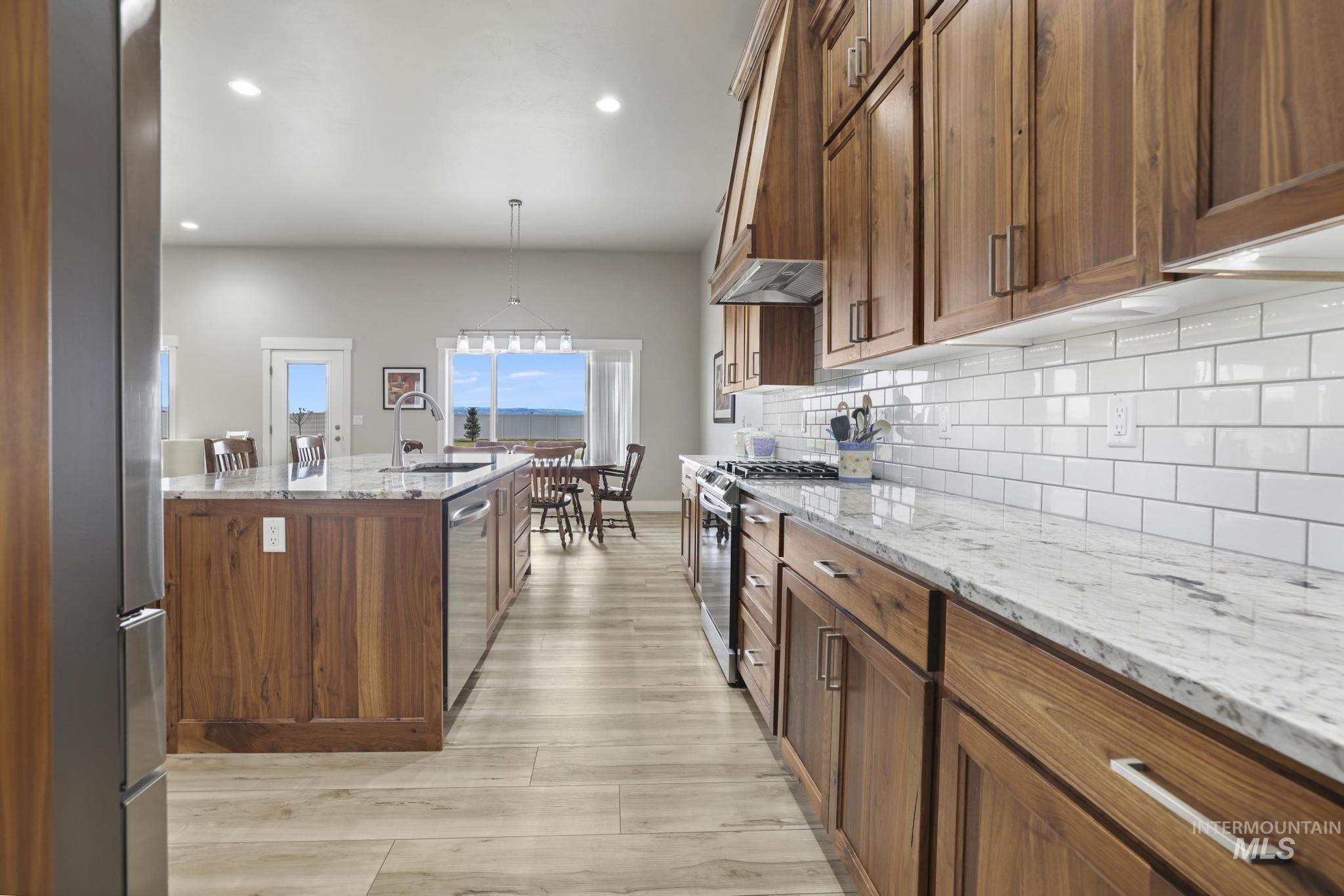 Kitchen with light stone counters, brown cabinets, appliances with stainless steel finishes, pendant lighting, and light wood finished floors