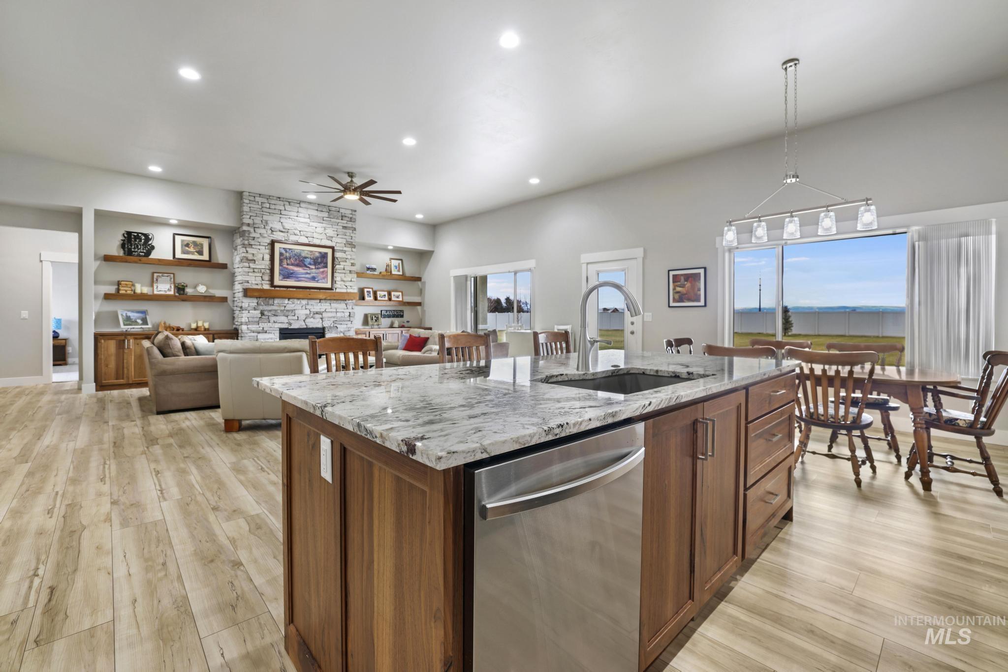 Kitchen featuring light stone countertops, light wood-style flooring, dishwasher, pendant lighting, and an island with sink