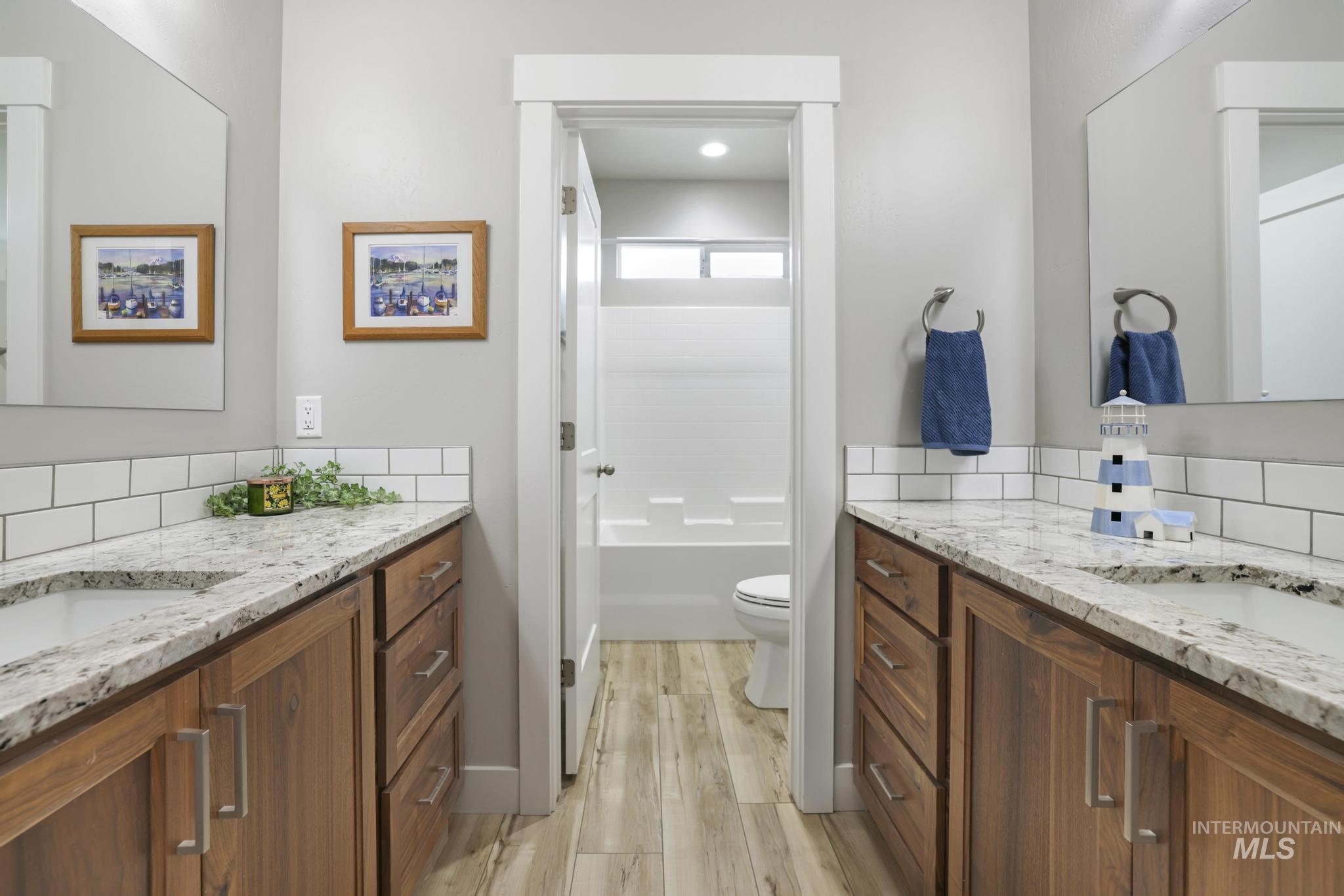 Bathroom featuring two vanities, light wood-style flooring, bathtub / shower combination, and backsplash