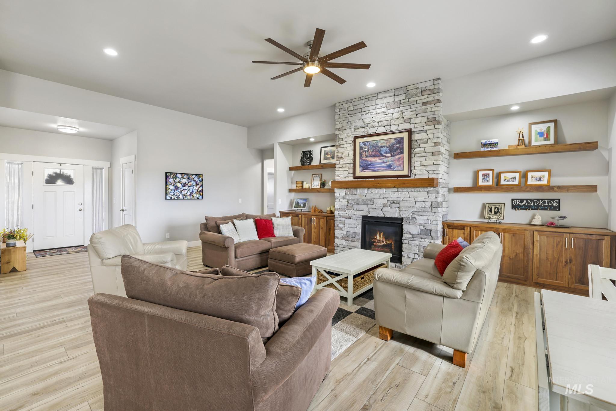 Living area featuring a ceiling fan, a stone fireplace, light wood-style flooring, and recessed lighting