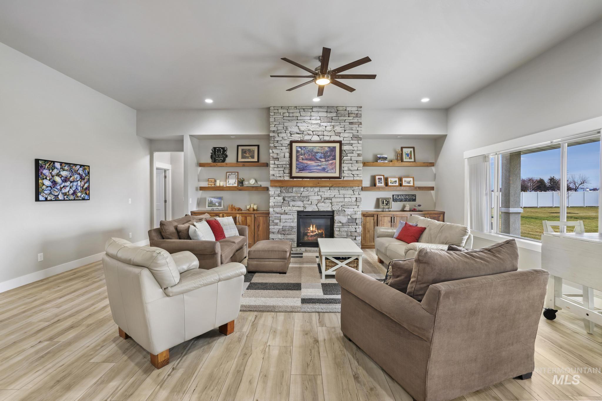 Living room with a stone fireplace, ceiling fan, light wood-style flooring, and recessed lighting