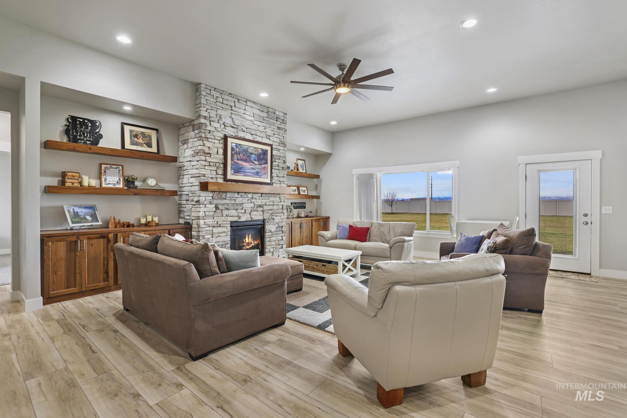 Living room with light wood-style floors, a fireplace, a ceiling fan, built in shelves, and recessed lighting