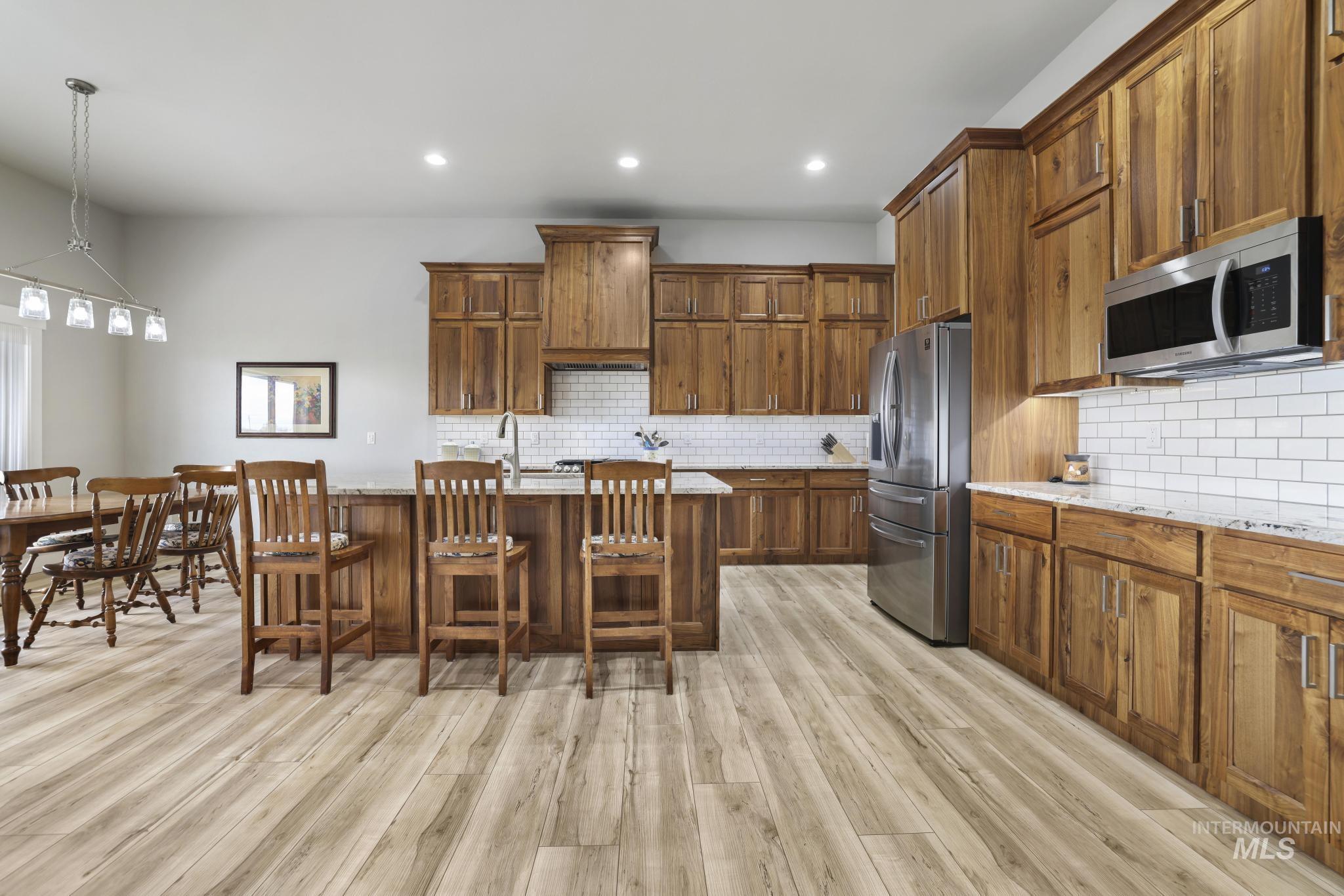 Kitchen with an island with sink, brown cabinets, recessed lighting, stainless steel appliances, and pendant lighting