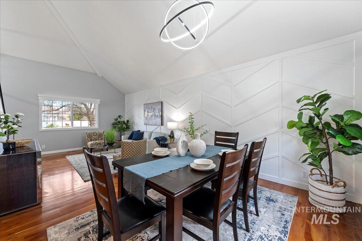 Dining area featuring an accent wall, lofted ceiling, dark wood-style flooring, a chandelier, and a decorative wall