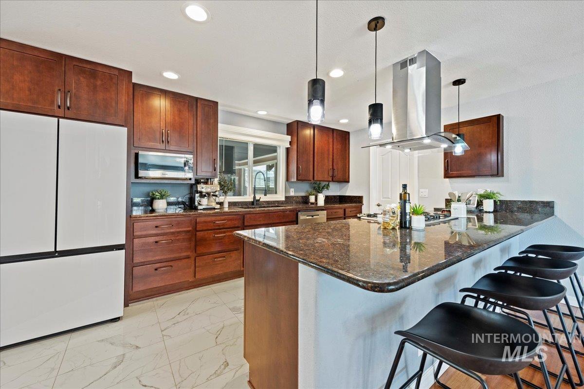 Kitchen featuring a peninsula, stainless steel appliances, dark stone counters, a kitchen breakfast bar, and light marble finish flooring