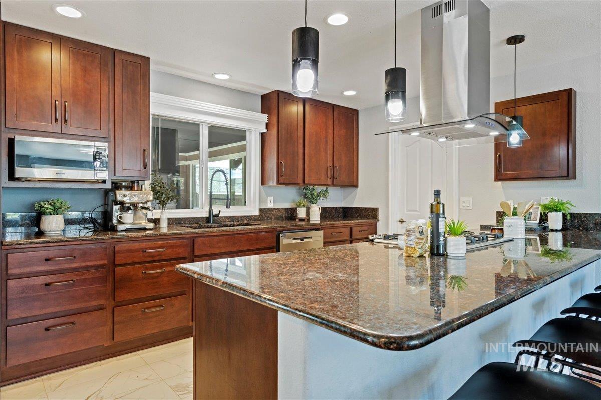 Kitchen with dark stone counters, island exhaust hood, a peninsula, hanging light fixtures, and stainless steel appliances