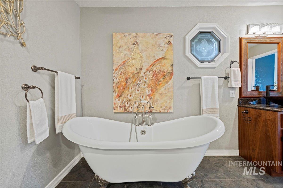 Bathroom with a freestanding bath, vanity, a textured wall, and dark tile patterned flooring