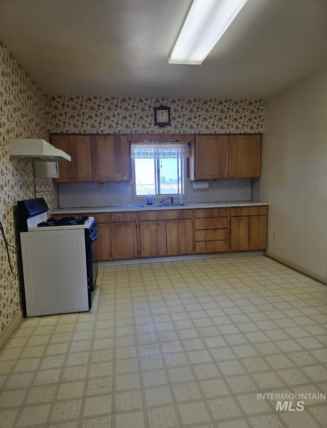 Kitchen with light flooring, gas range gas stove, brown cabinetry, light countertops, and under cabinet range hood