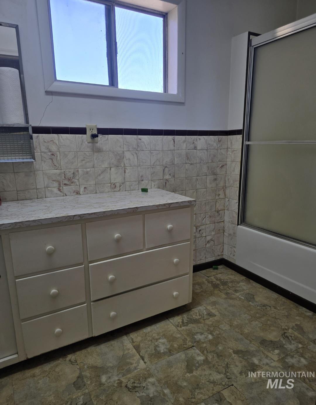 Bathroom with enclosed tub / shower combo, plenty of natural light, vanity, a wainscoted wall, and tile walls