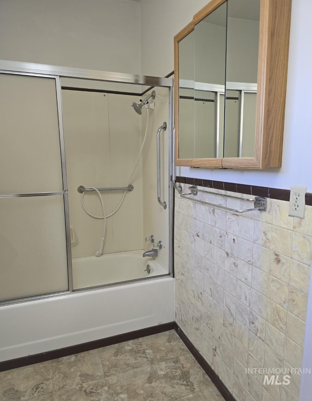 Bathroom with bath / shower combo with glass door, wainscoting, and tile walls
