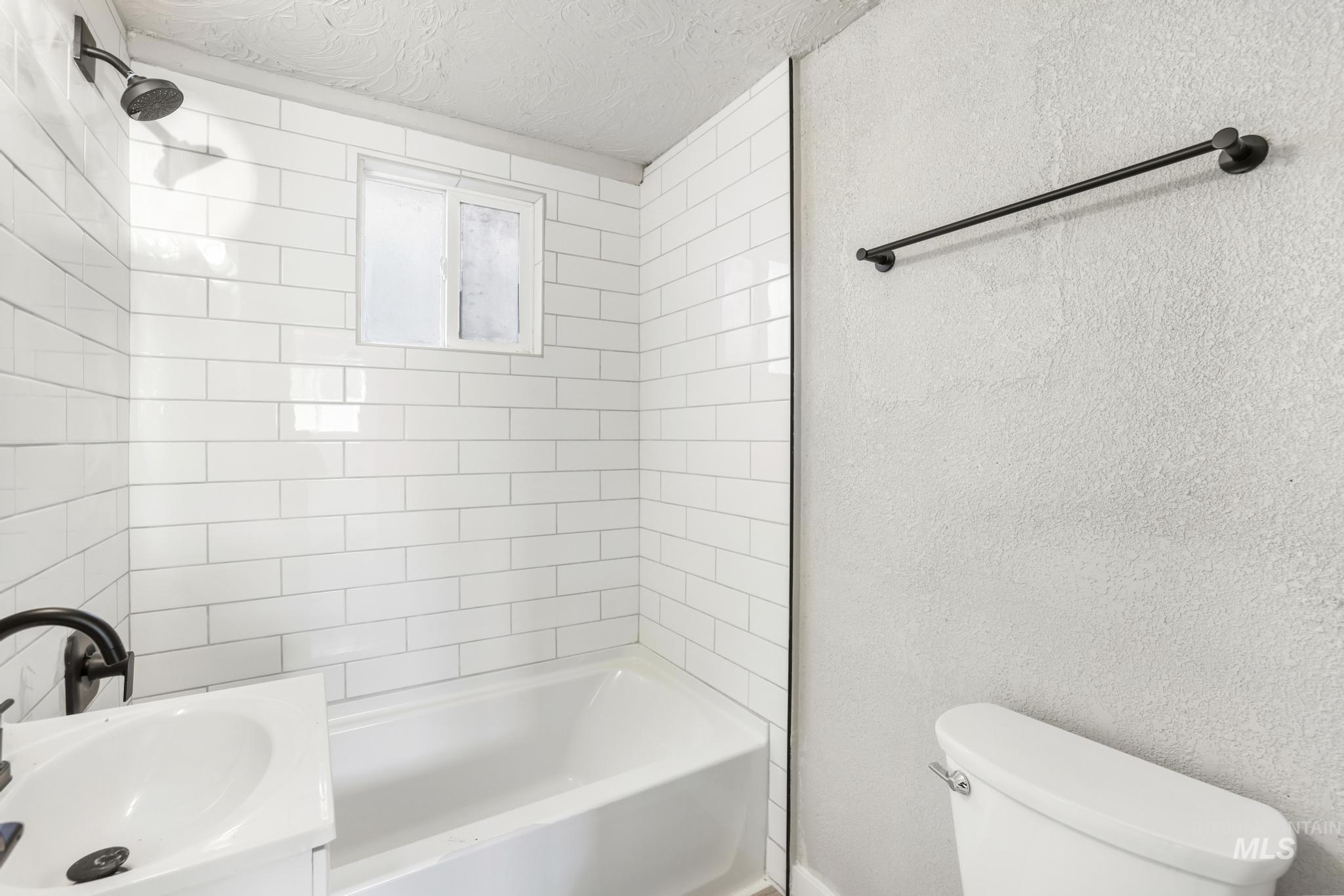Bathroom with a textured wall, bathing tub / shower combination, vanity, and a textured ceiling